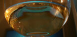 Halb gefülltes Weissweinglas vor blauem Hintergrund