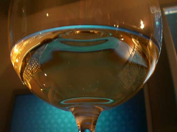Halb gefülltes Weissweinglas vor blauem Hintergrund