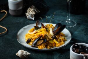 Teller mit Meeresfrüchte-Paella auf einem Tisch im Hintergrund Weingläser