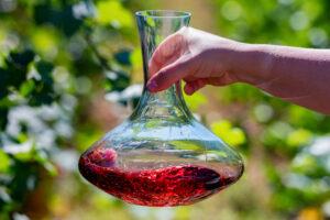 Hand hält und schwenkt Dekanter mit Rotwein