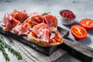 Weißbrot mit Tomaten und luftgetrocknetem Scheiben von Jamon Iberico Schinken auf einem Holzbrett.