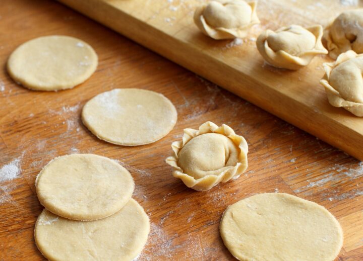 Runde Teigausschnitte und ein fertiges Pelmeni auf Holzbrett