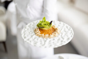 Koch hält einen Teller mit einem köstlichen vegetarischen Gericht, das mit einer Blume aus Avocado dekoriert ist, im Restaurant der gehobenen Küche. Nahaufnahme des Gerichts.