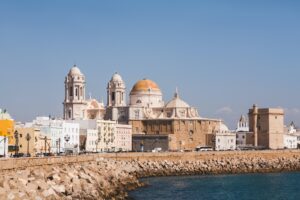 Kathedrale von Cádiz vor blauem Himmel. Im Vordergrund ein Kai.